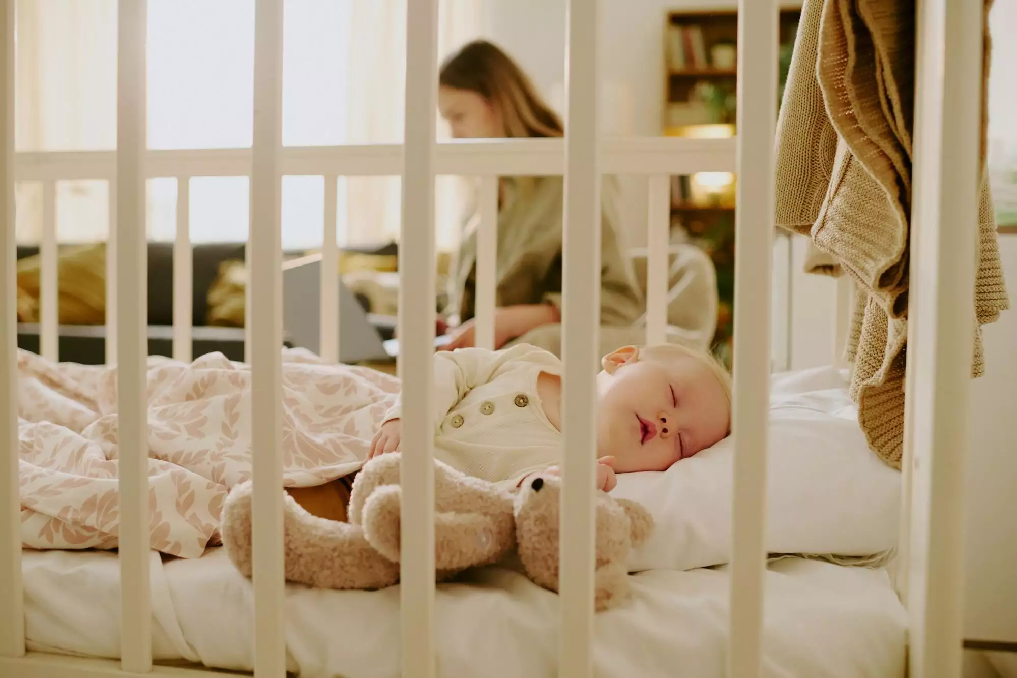 Sleeping Baby in Crib with Parent Working in Background